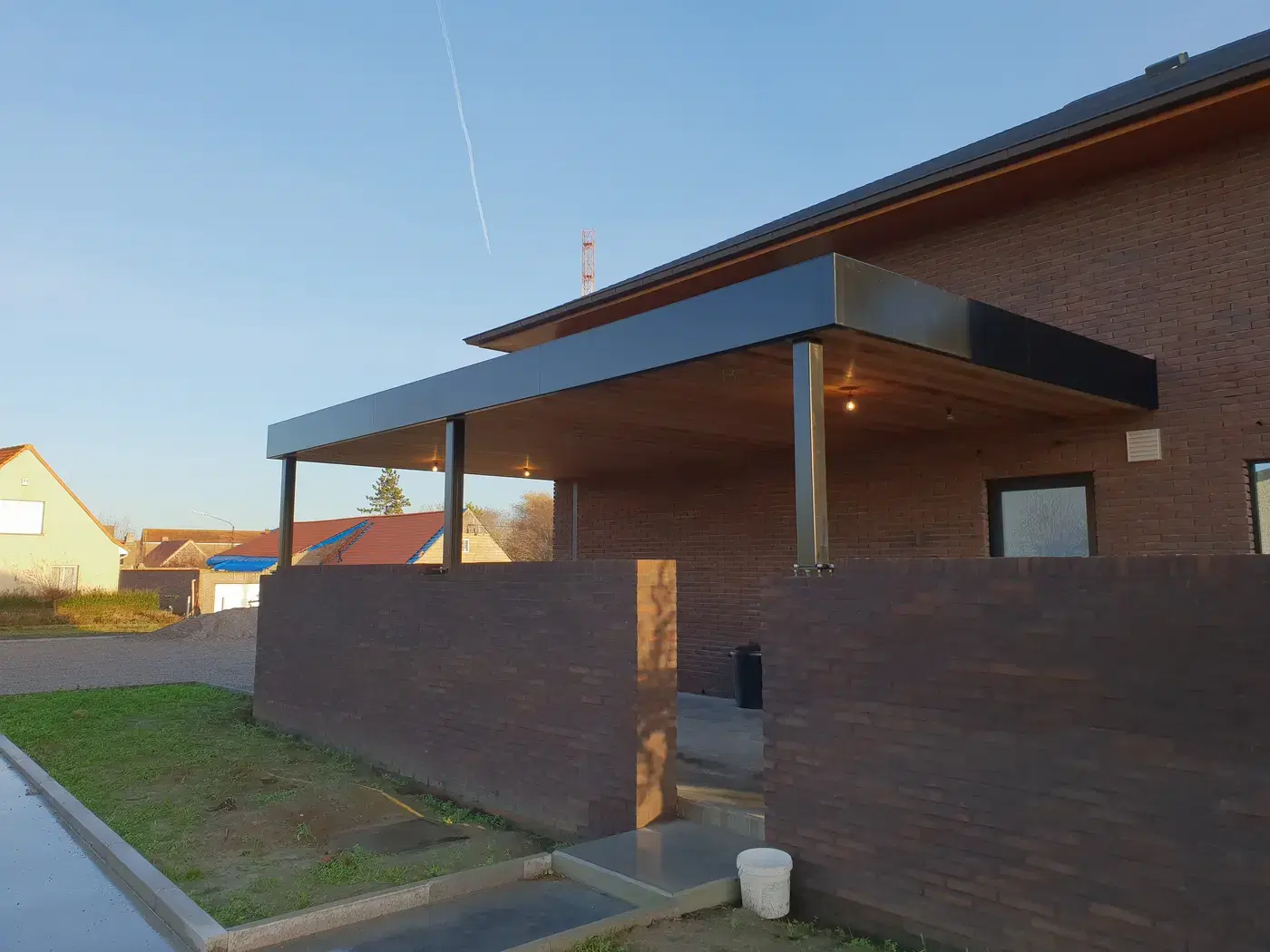 Zwarte stalen carport met houten plafond in gouden avondlicht