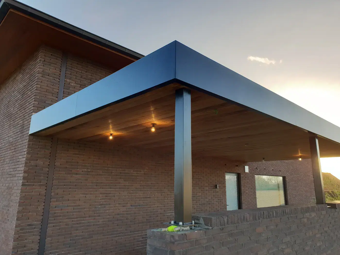 Zwarte staalstructuur en houten plafond van een carport, gezien vanaf de hoek
