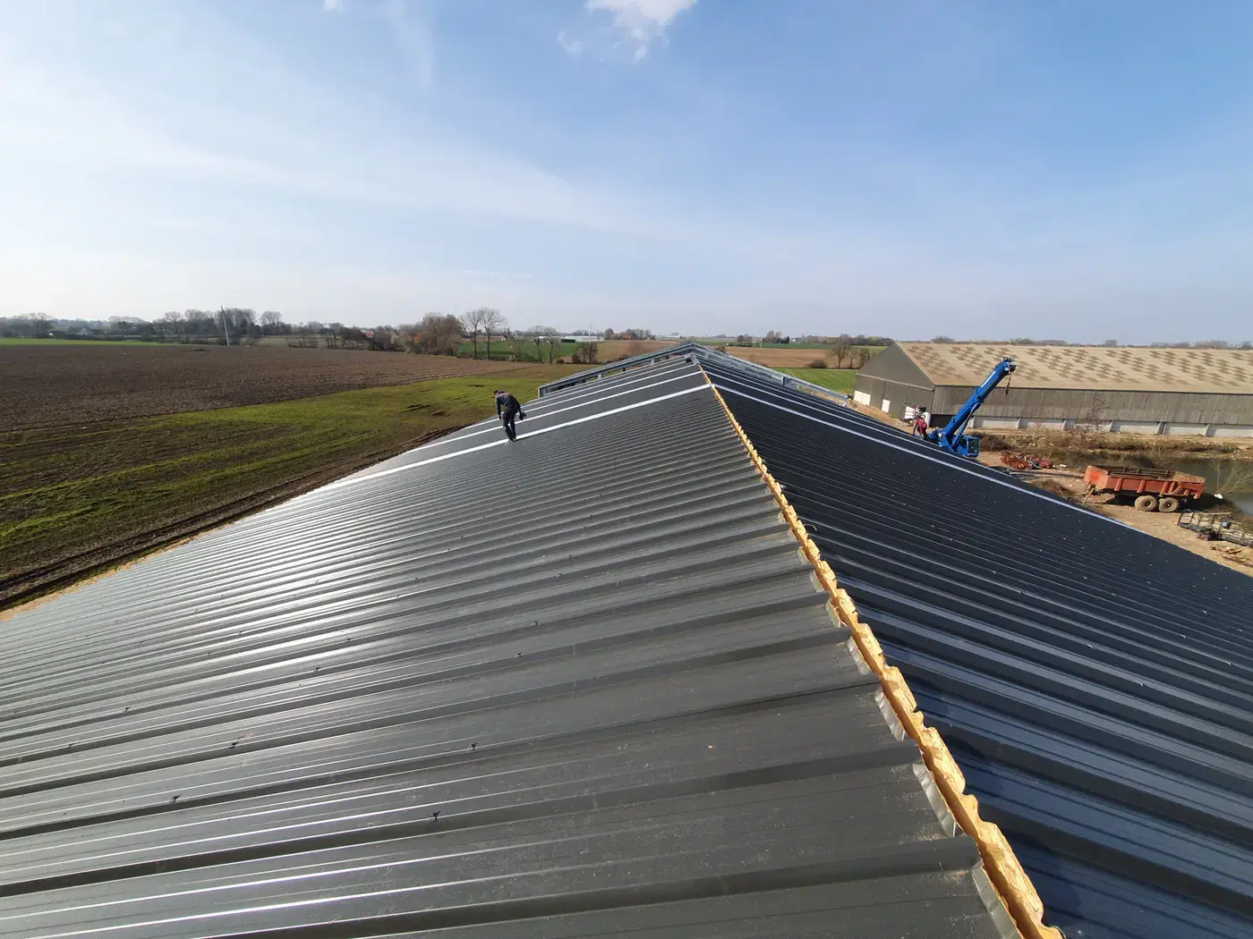 Vakman aan het werk op de nok van een lang stalen dak in aanbouw