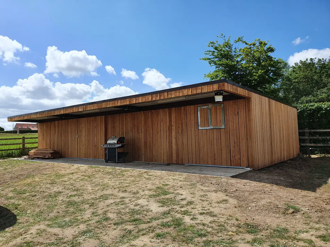 Afgewerkte loods met verticale houten gevelbekleding onder een strakblauwe zomerlucht