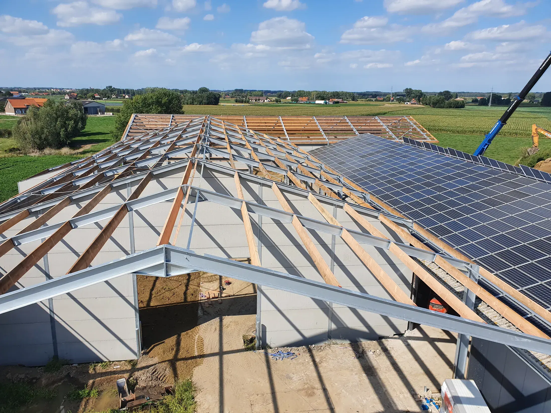 Dakstructuur in staal en hout met zonnepanelen, gezien van bovenaf in het Vlaamse landschap