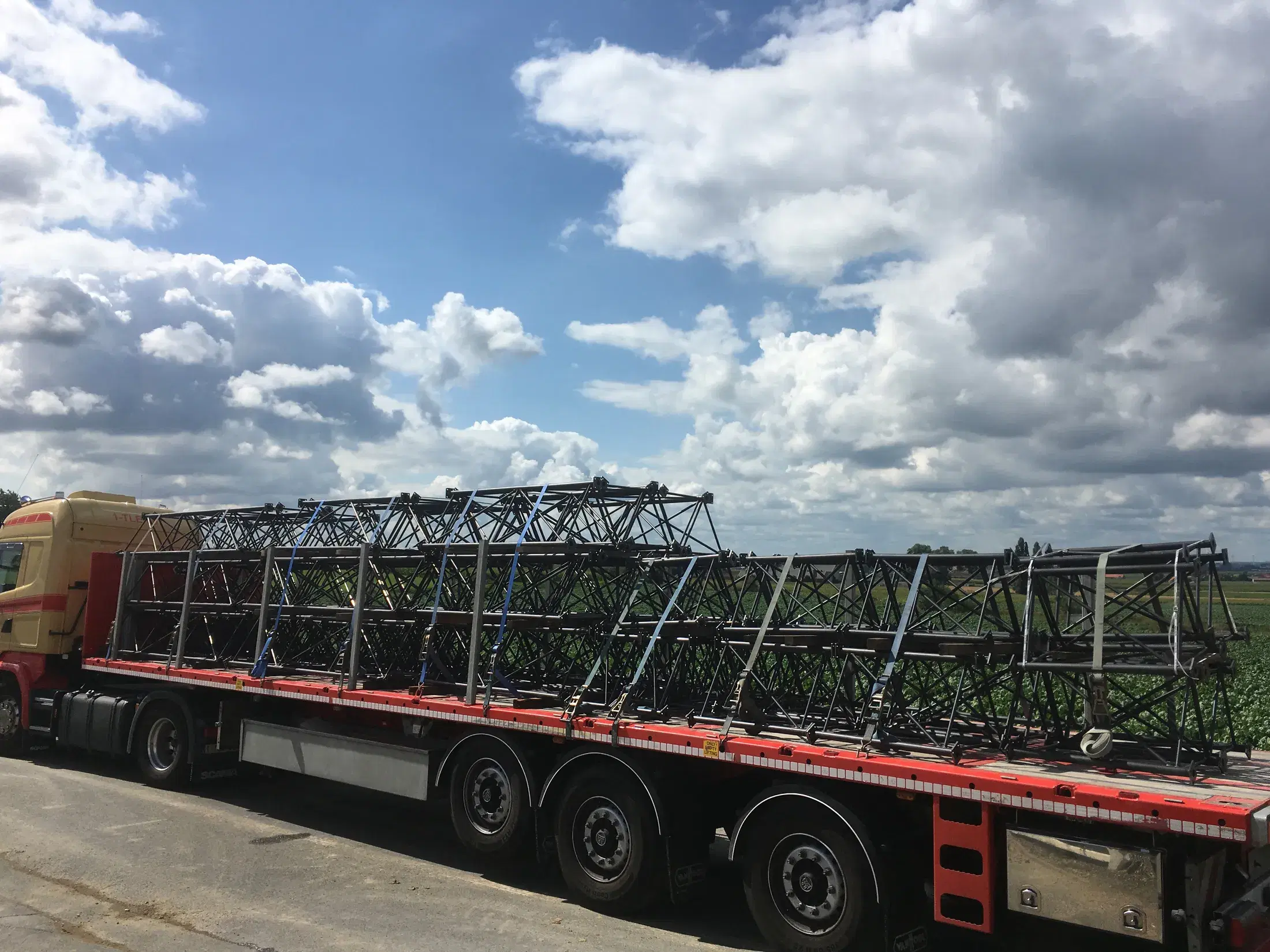 Vrachtwagen geladen met zwarte gelaste vakwerkliggers onder een blauwe wolkenlucht