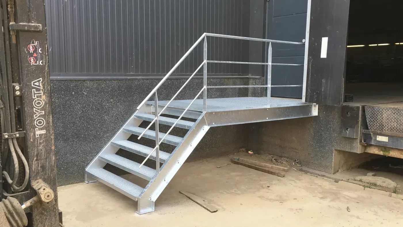 Strakke verzinkte staaltrap met bordes en leuningen aan een modern bedrijfsgebouw