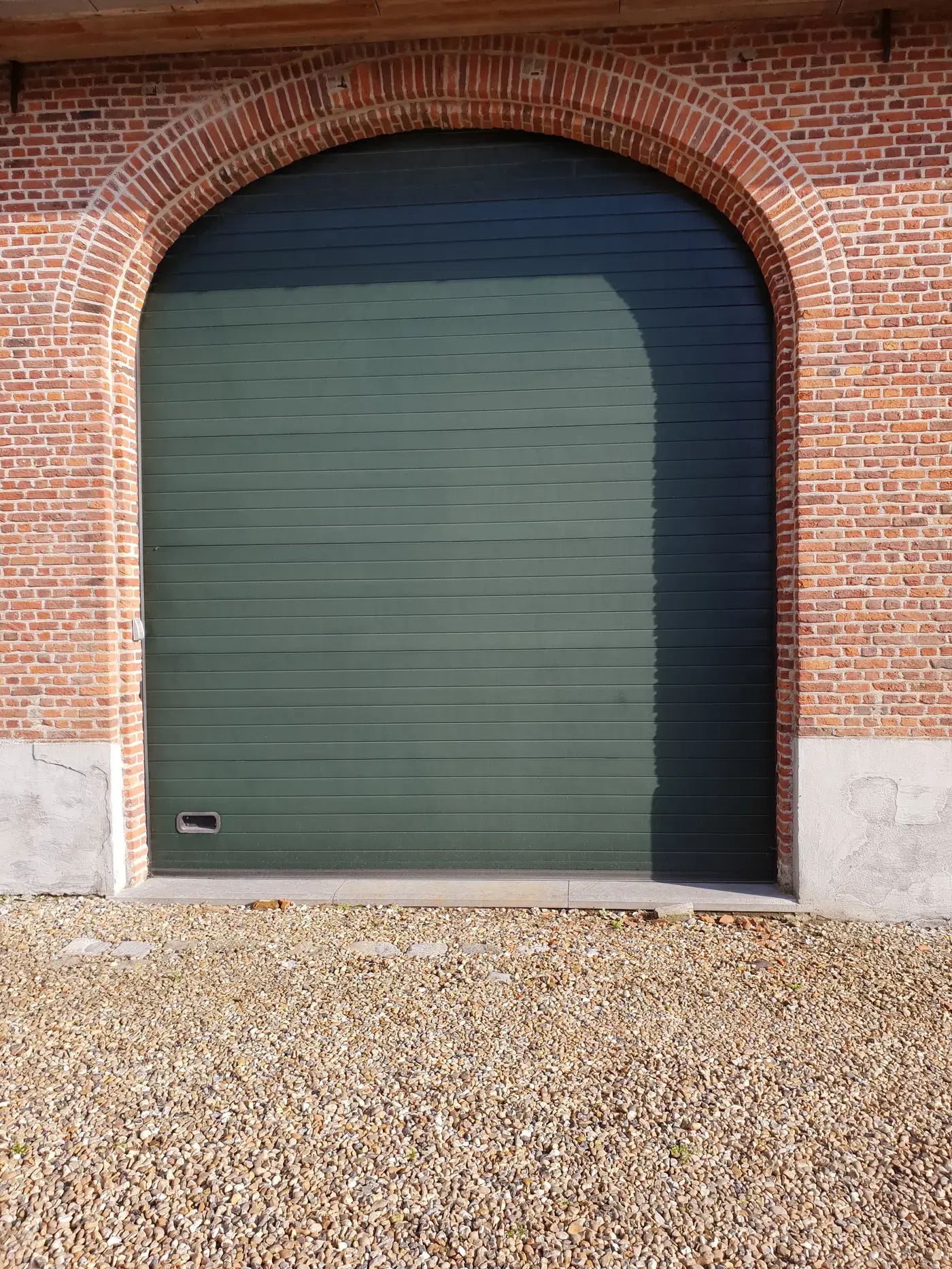 Groene garagepoort onder een boogvormige baksteengevel